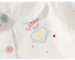 Close-up of white shirt with heart embroidery, carry on text and colorful buttons