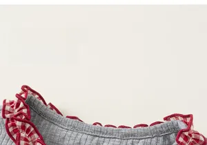 Detail of grey knitted top featuring red plaid ruffled collar and ribbed texture fabric
