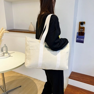Detail einer beigen Canvas-Tragetasche mit grünem Simple-Aufdruck und weißen Schultergurten