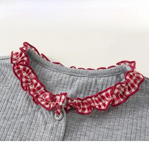 Close-up of girls' grey ribbed top featuring a red plaid ruffle collar and button detail
