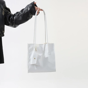 Detail of white lychee pattern tote bag with gold buckle and mini charm accessory