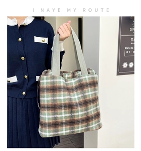 Detailed side view of a green tweed woven tote bag with plaid pattern on a model shoulder