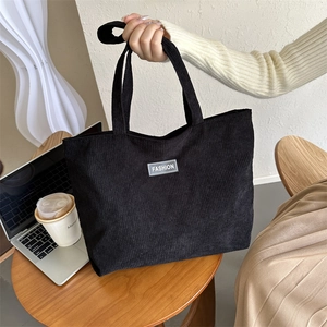 Detail of black corduroy tote bag with Fashion label on a wooden table setting