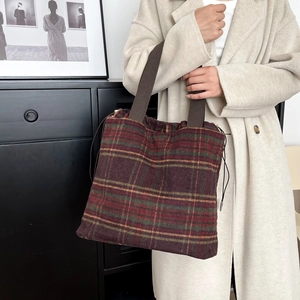Close-up of wool plaid tote bag with drawstring closure held by model in beige coat