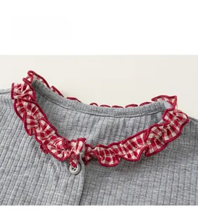 Detail showing grey ribbed fabric neckline with red plaid ruffle and grey button
