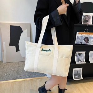 Detail einer cremefarbenen Canvas-Tasche mit Simple-Textprint zum schwarzen Blazer