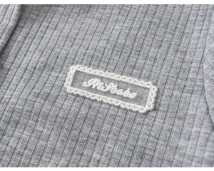 Detail of grey ribbed knit fabric with lace patch and Mr Baby embroidery design