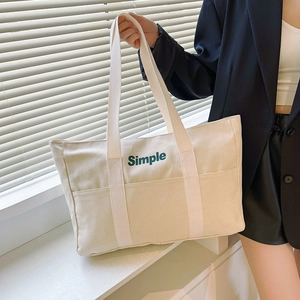 Detailansicht der cremefarbenen Canvas-Tragetasche mit Simple-Textdruck und breitem Gurt