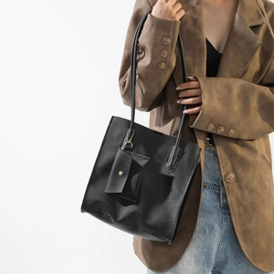 Minimalist black pebbled faux leather tote bag with matching pouch on a model's shoulder
