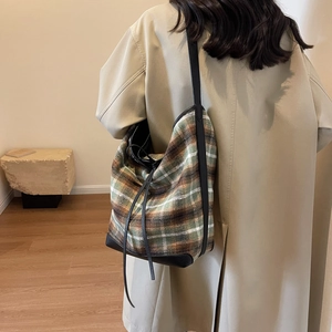 Detailed back view of a plaid wool tote bag with leather straps on a beige coat model