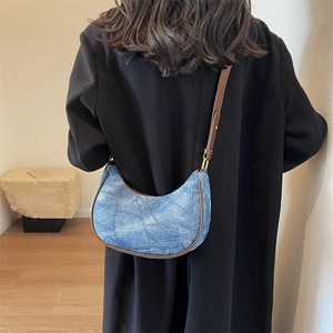 Sac demi-lune en denim bleu avec garniture en cuir marron porté sur un manteau noir