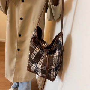 Detail of vintage brown plaid wool tote bag with leather trim on beige trench coat