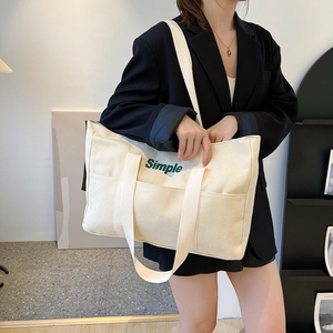 Detailansicht der cremefarbenen Canvas-Tasche mit grünem Simple-Schriftzug und Seitentaschen