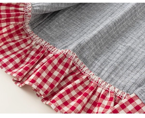 Detail of grey ribbed fabric stitched with red gingham pleated trim and fine white stitching