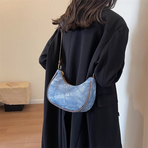 Détail du sac hobo en jean bleu avec garniture en cuir marron et finitions dorées