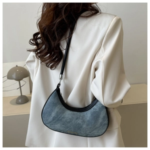 Model wearing a crescent denim underarm bag with black leather trim and silver buckles