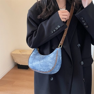 Détail du sac demi-lune en denim bleu avec coutures géométriques et bandoulière en cuir brun