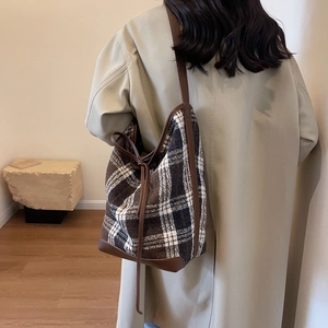 Detail of checkered wool tote bag with brown leather straps on a beige trench coat