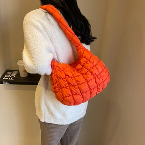 Side view of woman carrying orange quilted puffer bag with matching padded shoulder strap