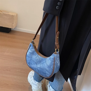 Détail du sac hobo en denim bleu avec garniture en cuir brun et fermeture dorée