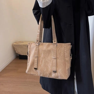 Detail view of beige tote bag with pleated texture and adjustable strap on a model