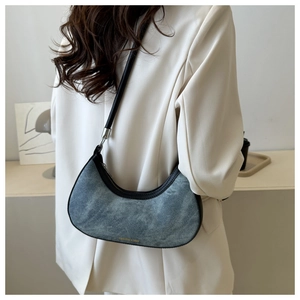 Detail of denim underarm bag with black leather trim and golden fashion logo on a white blazer