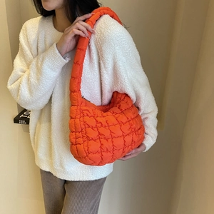 Vibrant orange quilted shoulder bag shown on model with white sweater and zipper detail