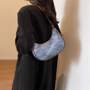 Détail du sac croissant en denim bleu avec garniture en cuir marron porté par un mannequin