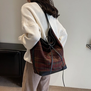 Detail of red-brown checkered wool tote bag with black leather base shown on a shoulder