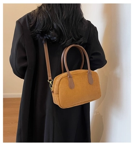 Detail of a brown suede Boston bag with leather handles and gold metal hardware