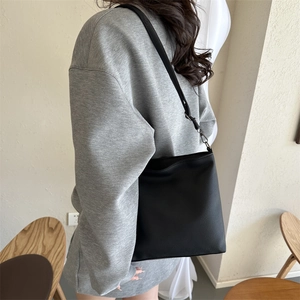 Detail of minimalist black lychee grain PU leather crossbody bag worn on a shoulder