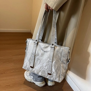 Detail of silver tote bag with metallic crinkle texture and slim shoulder straps on model