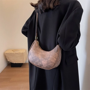 Sac hobo marron à texture vintage porté sur un manteau noir dans un décor moderne