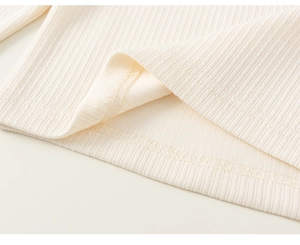 Détail de la texture en maille côtelée crème et des coutures de l'ourlet sur la robe de fille
