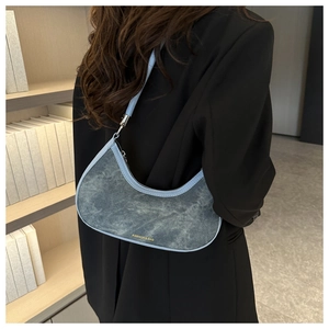 Detail view of denim half-moon underarm bag on model with blue leather shoulder strap