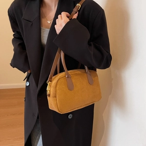 Chic mustard yellow suede Boston bag with brown leather handles worn by a model