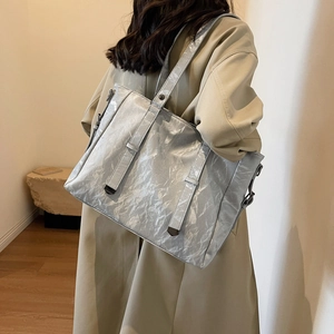Detail of silver pleated tote bag with metallic texture and sleek metal shoulder strap hooks