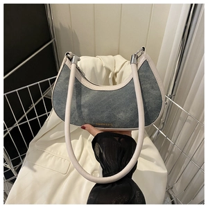 Detail view of denim crescent shoulder bag with cream leather trim in a metal basket