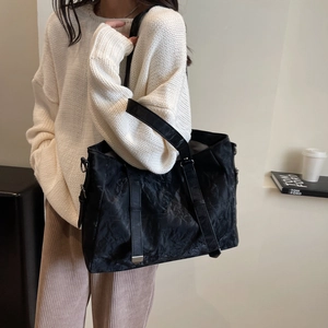 Detail of black pleated tote bag with double handles and long strap shown on model