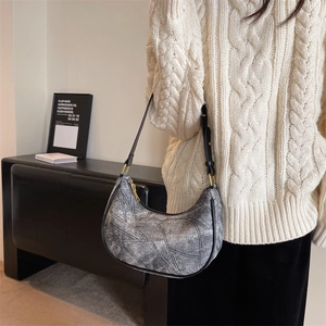 Détail d'un sac hobo en similicuir gris avec patchwork sur un pull en maille torsadée