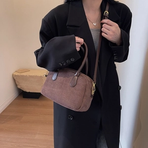 Detail of dark brown suede crossbody pillow bag with polished handles and gold hardware