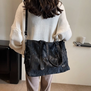 Detailed view of black pleated tote bag with adjustable strap and textured surface