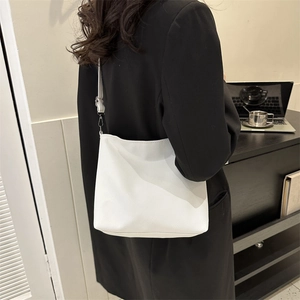 White minimalist bucket bag with adjustable strap worn by model in a modern office setting