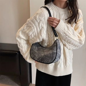 Détail d'un sac bandoulière croissant gris foncé avec texture cousue sur pull blanc