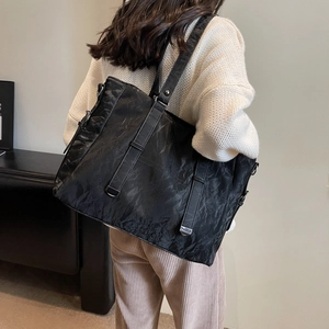 Minimalist black tote bag with unique pleated texture and wide shoulder strap