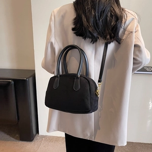 Minimalist black matte crossbody bag worn over a grey blazer with golden metal clasp