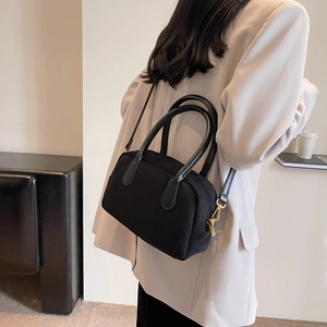 Detail view of a black suede handbag featuring dual circular handles and gold hardware