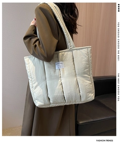 Close-up of beige quilted puffer tote bag with stitched logo label worn with brown blazer