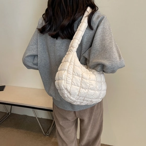 Close-up of white quilted shoulder bag made of lightweight fabric worn by a female model