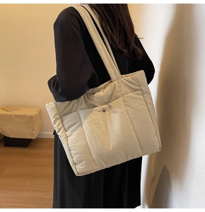 Detail of beige quilted tote bag showing padded texture and front pocket with snap button
